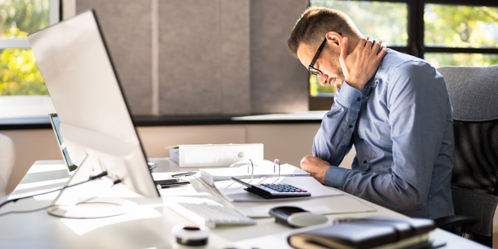 MedLife - hombre en oficina con dolor de cuello por mala postura, destacando la importancia de la ergonomía para prevenir lesiones laborales
